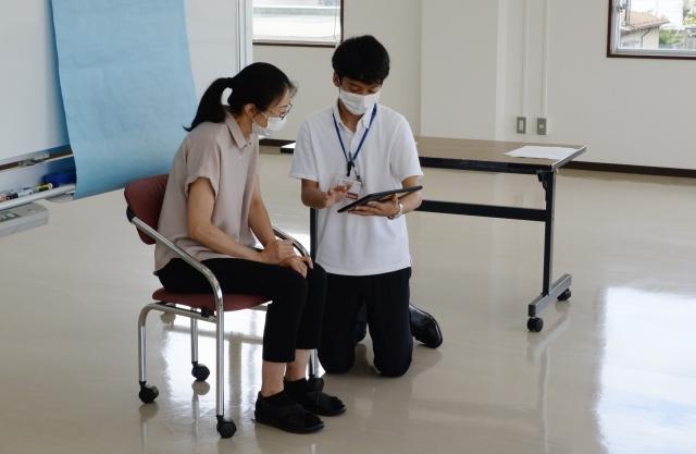 椅子に座っている女性に撮影した顔写真をタブレットの画面で見せている職員の写真
