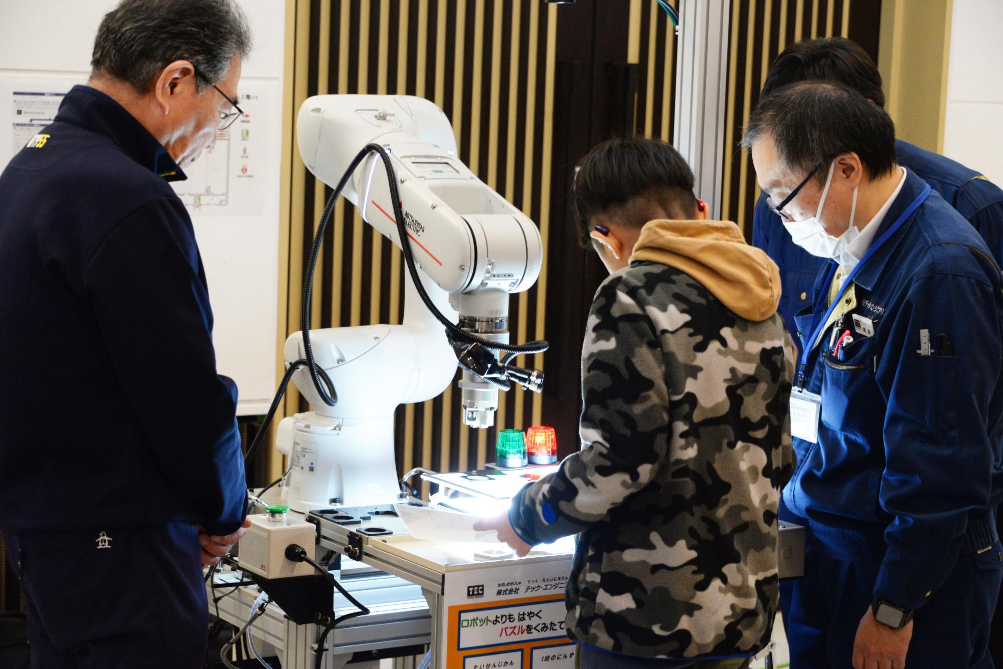 ロボットを動かす体験をする子どもと操作を説明する社員