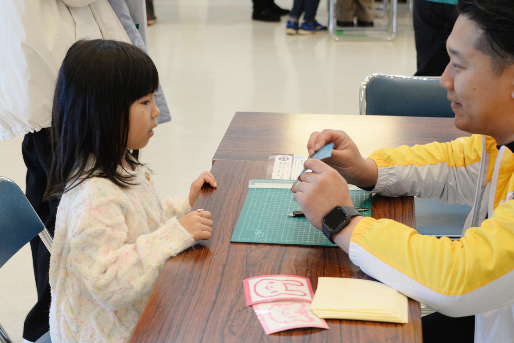 絵を切り抜く体験の説明を受ける子どもと説明するスタッフ