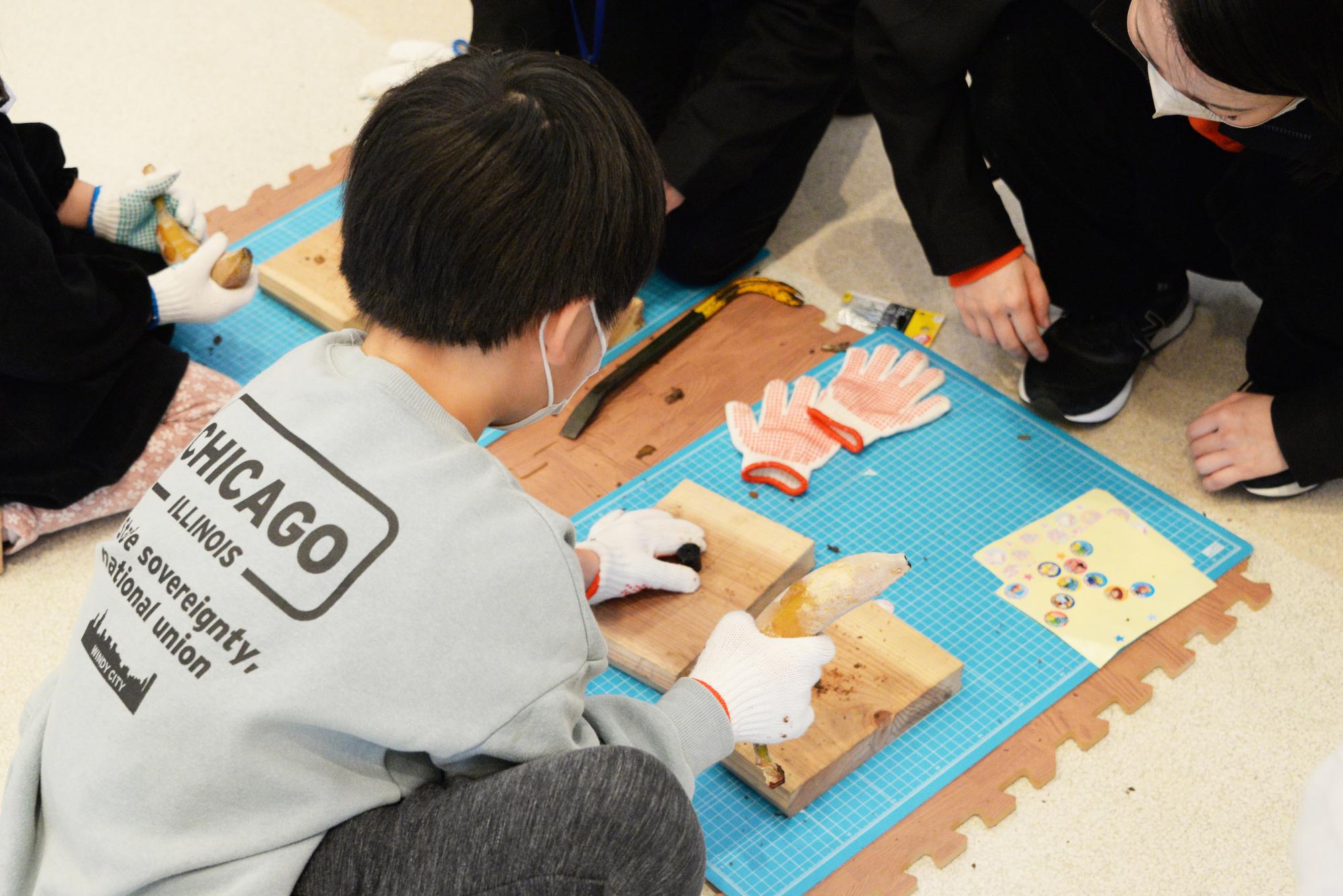 凍らせたバナナで釘をたたく子どもと様子を見ている社員