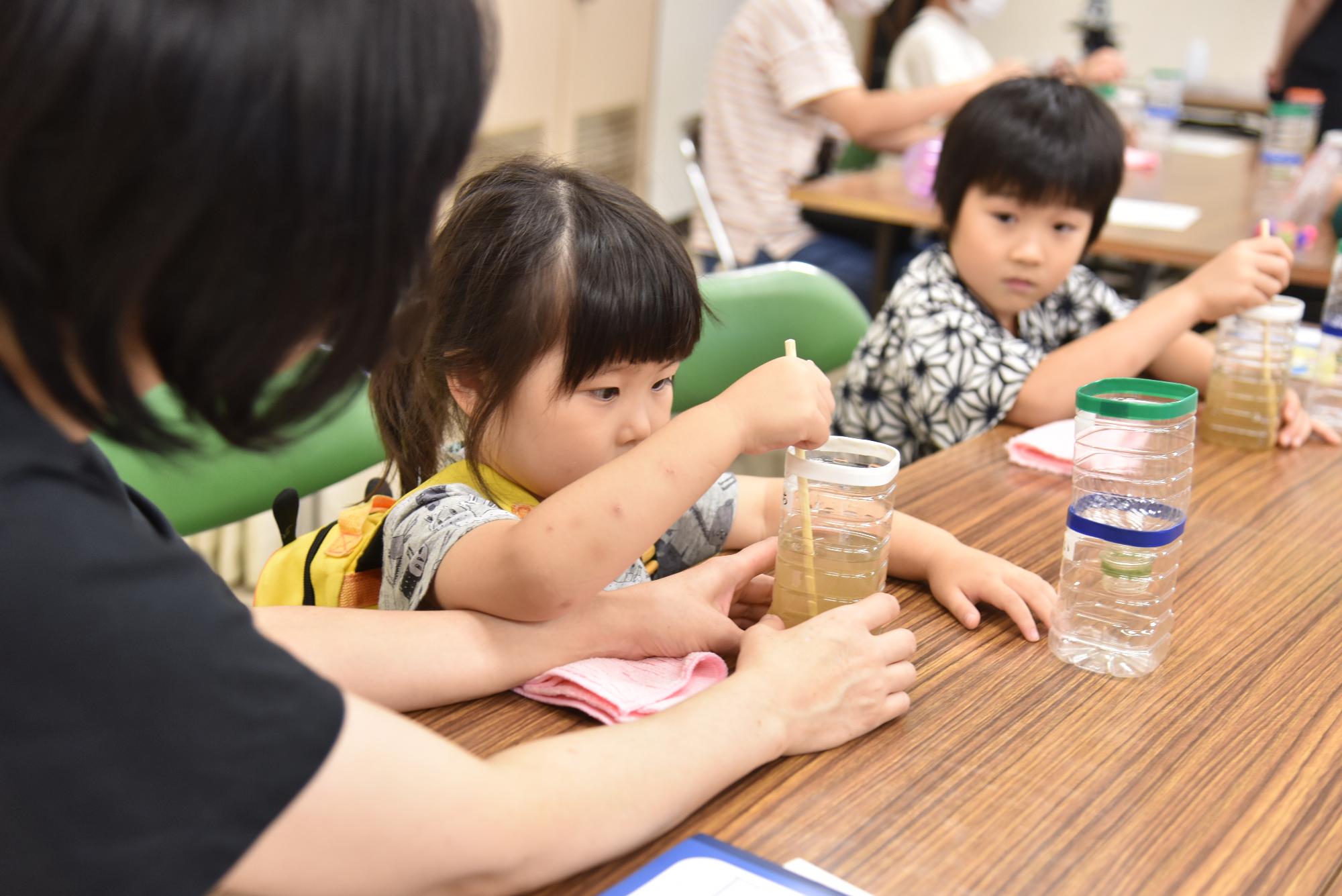 実験教室でボトルに入った水をかき混ぜる子どもたち