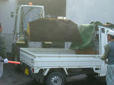 軽トラックの荷台に、ショベルカーで肥料を入れている写真