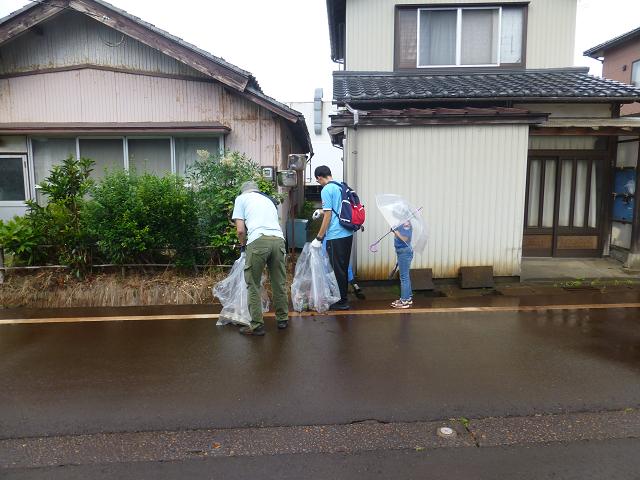 雨に濡れた道の脇で親子でゴミ拾いをする参加者の写真