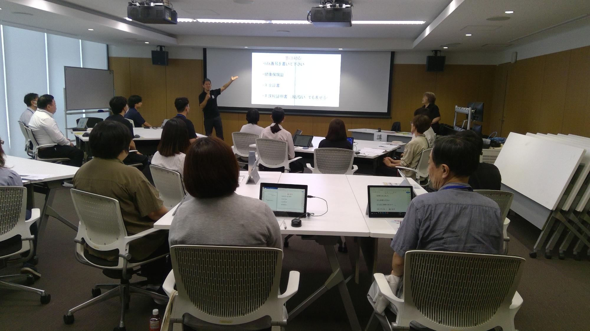 大きなスクリーン伝えたい内容が表示され、講師が説明している様子の写真