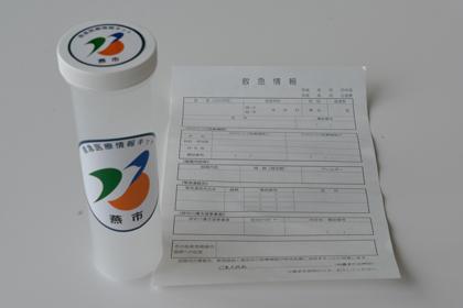 燕市のマークが使われている円柱状の救急医療情報キットと救急情報の用紙の写真