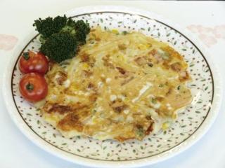 ミニトマト、ブロッコリーと一緒に盛り付けられた「チーズとマカロニのお好み焼き」の写真