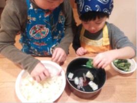 子ども2人が鍋に白菜やベーコンなどをいれている写真