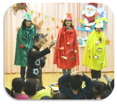 緑、赤、黄色の衣装を着た3名が舞台に立ち、その前で女性が話をしている写真