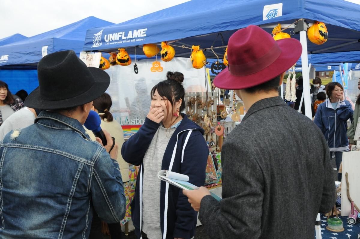 若い女性が、帽子を被り手にメモを持った複数の男性に話している写真