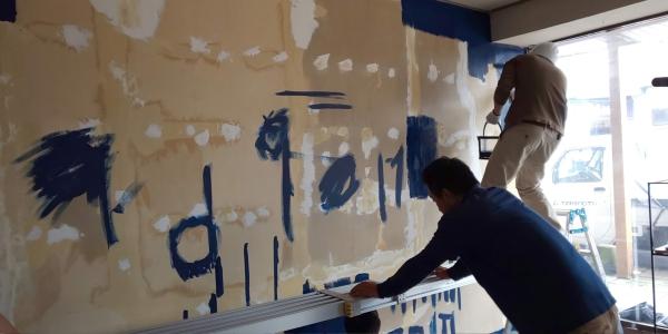広い壁面の端からペンキ塗りをしている男性の写真