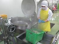黄色いエプロンをつけた作業者が食材を釜でゆでている写真