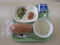 緑色のトレーに、おかずのお皿・牛乳・白いスープ・パックに入ったコッペパンが並べられている写真