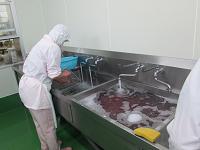 白衣の作業者が、流しに張った水で箸・スプーンを洗浄している写真