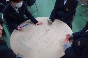 丸いテーブル「えんたくん」にカラフルなペンで文字を書く児童たちの写真