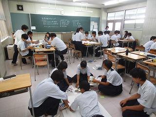 着席して話し合ったり、床で模造紙に書き込みをしたりしている生徒たちの写真