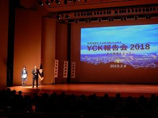 壇上に立って話している二人と、「YCK報告会2018」のスライドの写真