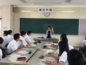 黒板の前で話をする女性の講師と、座って話を聞いている生徒たちの写真