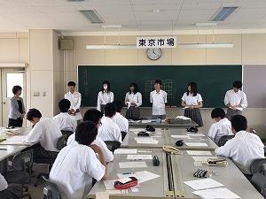 黒板の前に並んで発表をする生徒たちと、隣に立っている女性講師と、座っている生徒たちの写真