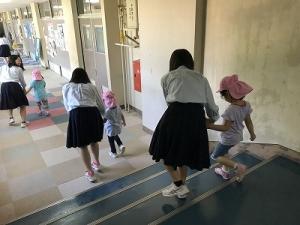 女子生徒たちが、保育園児たちと手をつないで廊下を歩いている写真