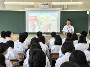黒板のスクリーンに表示した地図を説明している講師と、座っている生徒たちの写真