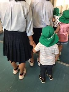 緑の帽子をかぶった園児の手を引いている女子生徒の写真