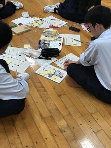 床に座って、手元の紙に付箋を張り付けている生徒たちの写真