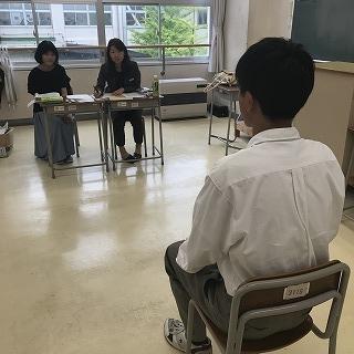 教室で、二人の女性の面接官と少し距離をとって座り、面接をしている男子生徒の写真