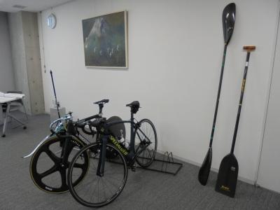 部屋の一角に自転車2台が置かれ、壁にカヌーの道具が2本立てかけられている写真