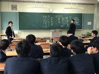 黒板の前に立っている男子生徒と、黒板の横で生徒を見ている講師と、前方を見ている男子生徒たちの写真