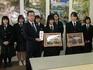 額縁に入った写真を持っている二人の女子生徒と、隣で目録の紙を持っている男性を、右斜め前方から撮影した写真