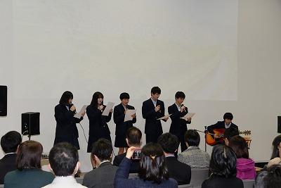 舞台に並んで歌っている生徒たちと、聞いている参加者たちの写真