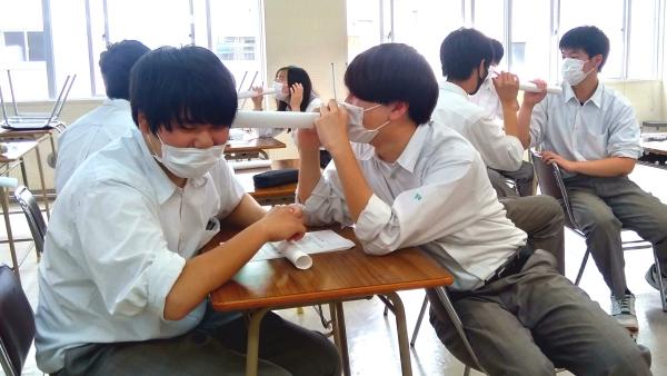 机ごしに、男子生徒が後ろの男子生徒の耳に紙の筒を当て、伝言ゲームをしている写真