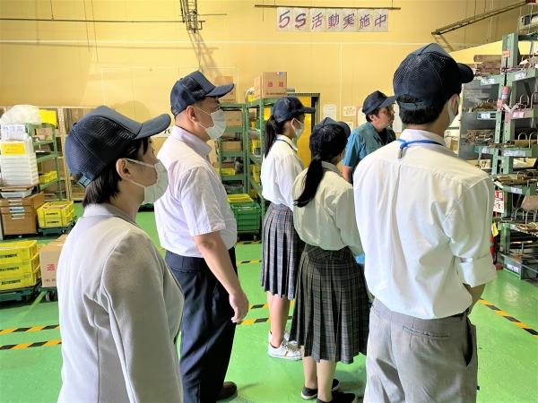 工場で、立って見学をしている生徒と関係者の写真