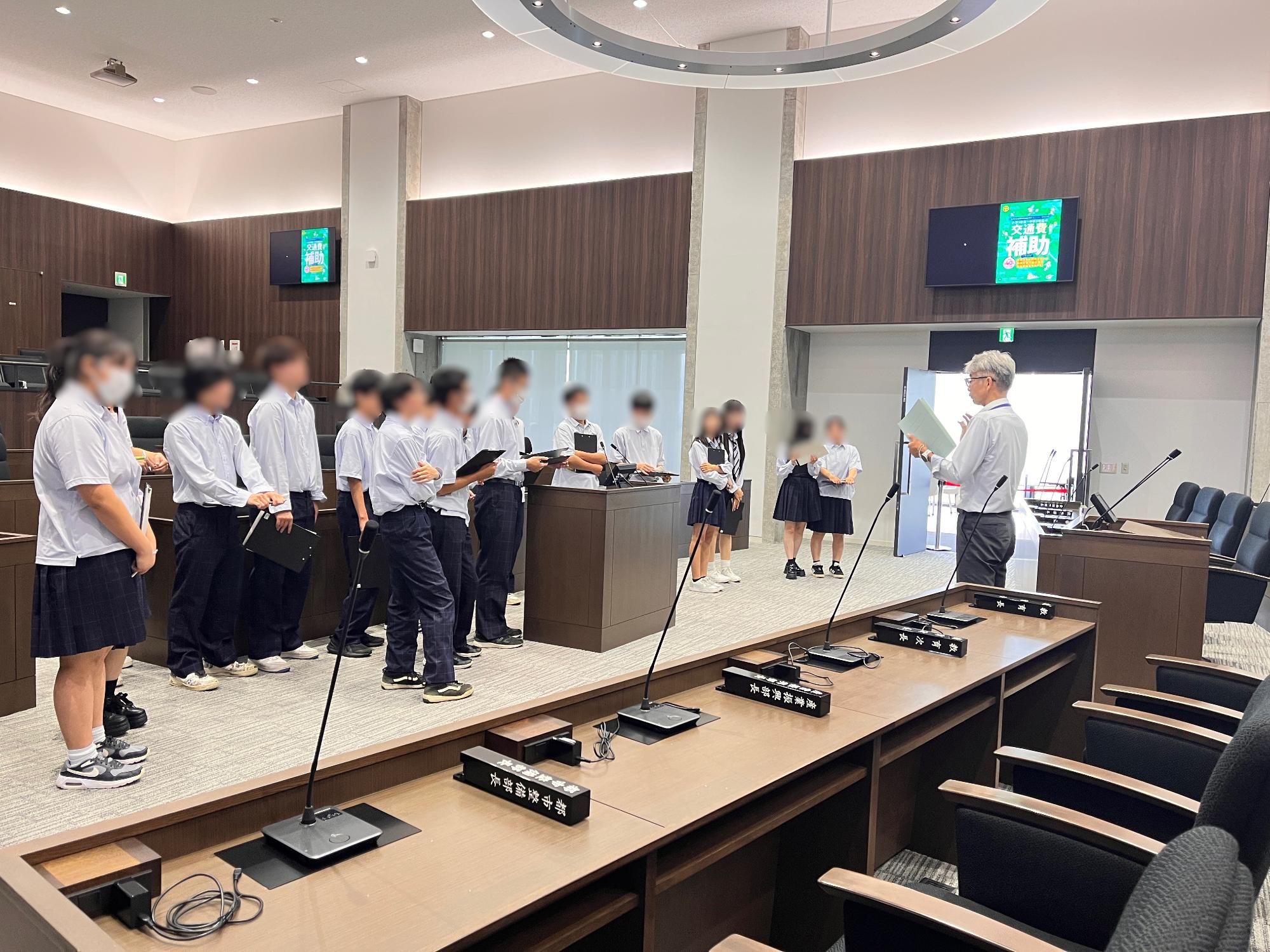 分水高校生が議場にて職員からの説明を聞いている写真。