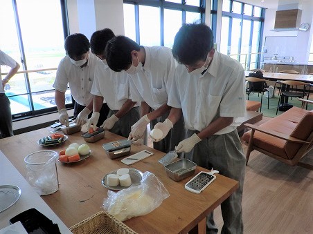 男子生徒3人と先生が野菜をキッチンスライサーで試し切りしている写真。