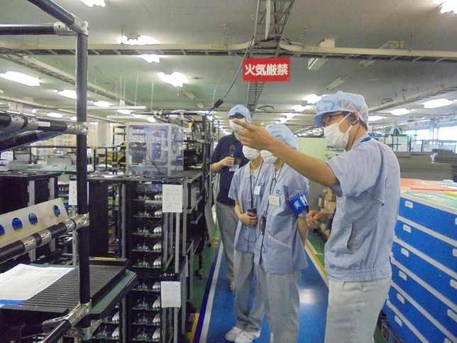 工場内の見学中に、生徒二人が工場内の装置の説明を受けているところ