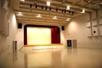 床には何も置かれておらず赤い緞帳のついた舞台がある大ホールの写真