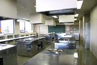 銀色の調理実習台が複数設置された調理室の写真