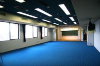 奥行きがあり床が青く、天井には蛍光灯が設置された視聴覚室の写真