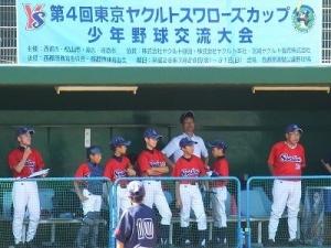 大会名が上部に書かれたベンチに上半身が赤いユニフォームを着た多数の野球選手がいる写真