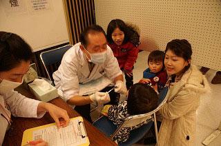 白衣を着た医師が児童の歯科検診をしている写真