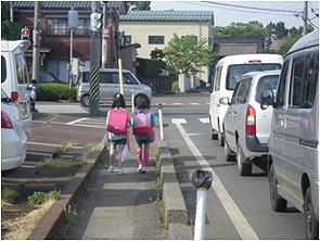 ピンク色のランドセルを背負った2人の児童が歩行者通路を歩いている後ろ姿の写真