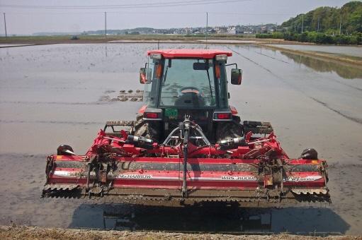 赤色の農耕機と広い水田の写真