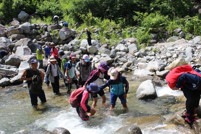 渓谷で足を水に浸しながら遊ぶ児童たちの写真