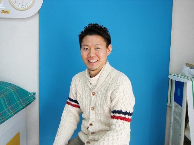 白いセーターを着てカメラに向かって微笑む岡崎真氏の写真