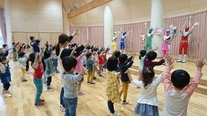 ステージの上で踊るキャラクターにあわせて児童たちが身体を動かしている写真