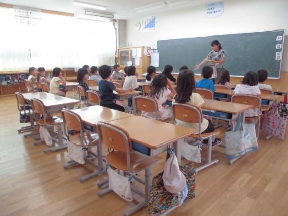 教室の黒板の前で話をしている女性と、座って聞いている子供たちの写真