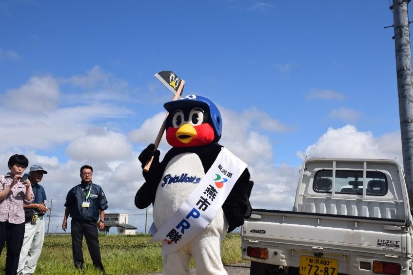 青空の下、つば九郎がポーズをとって立っている写真