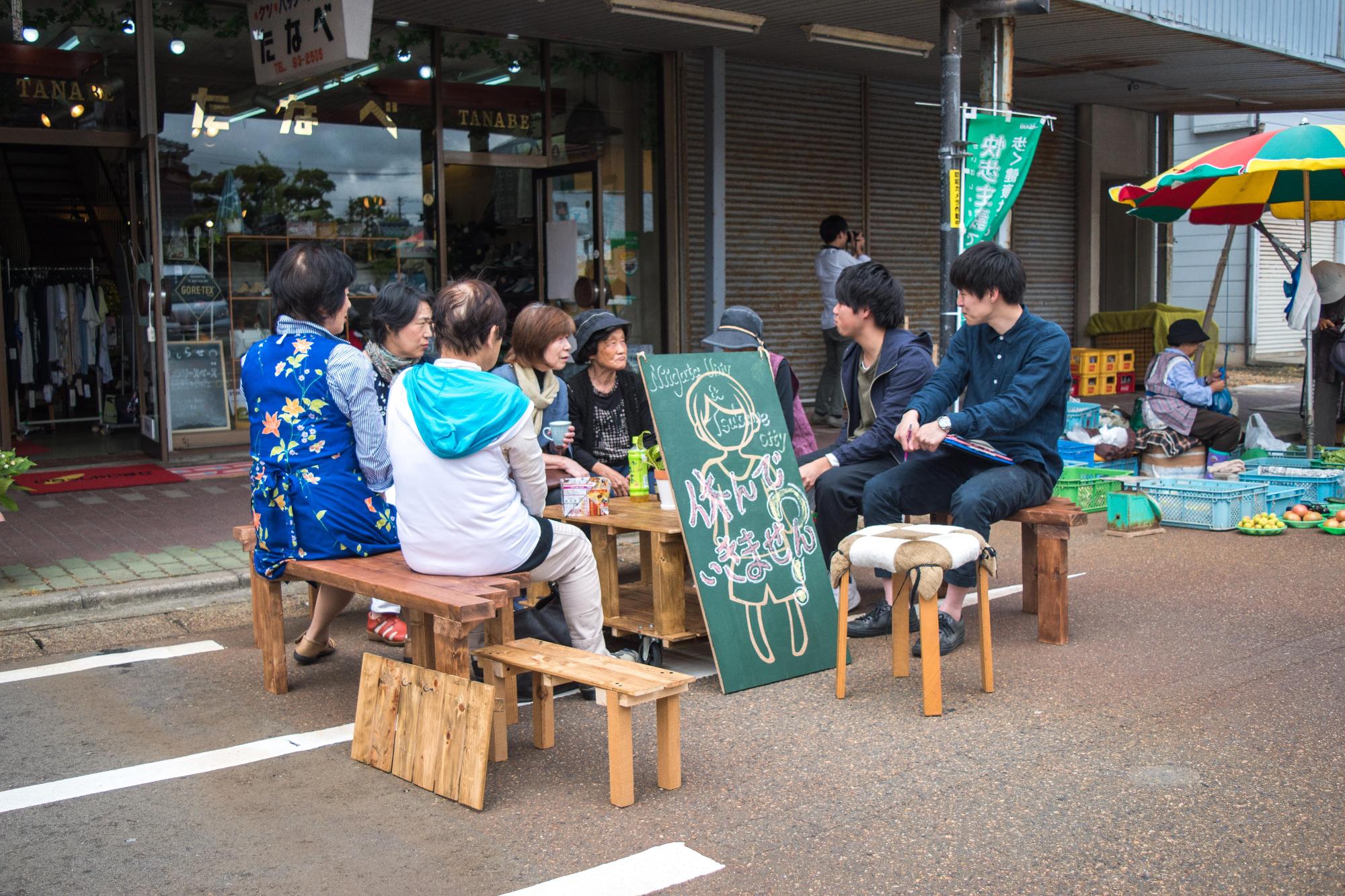 商店街のベンチに座ってお話する人たちの写真