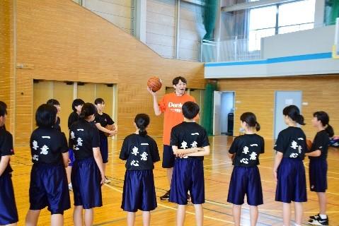 黒いシャツを着た子供たちと、バスケットボールを持ち上げているオレンジ色のシャツを着た男性の写真